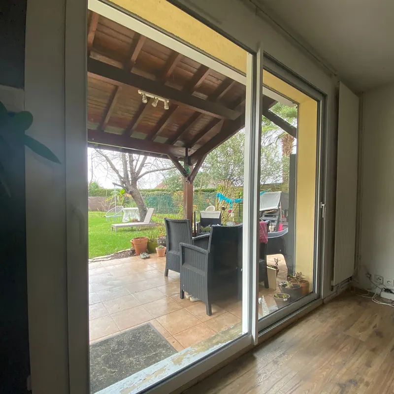 Grand coulissant 2 vantaux à cadre clair, vu du séjour, donnant sur une terrasse couverte et le jardin