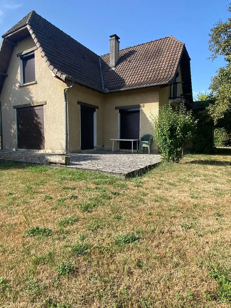 Maison à façade beige et toit de tuiles brunes, équipée de volets roulants noirs au rez-de-chaussée et à l’étage